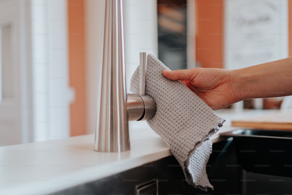 a hand is holding a cloth over a sink faucet