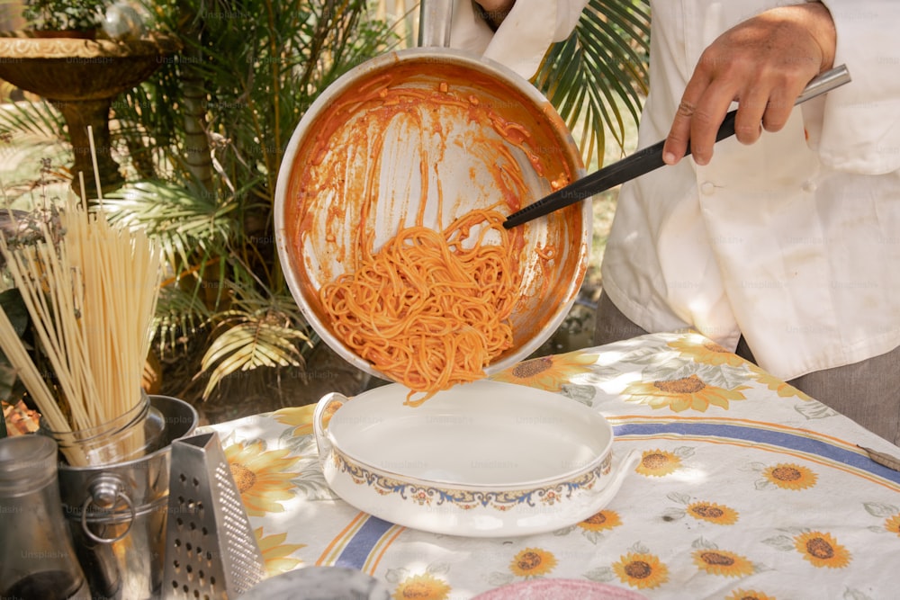 Una persona está cocinando fideos en una sartén sobre una mesa