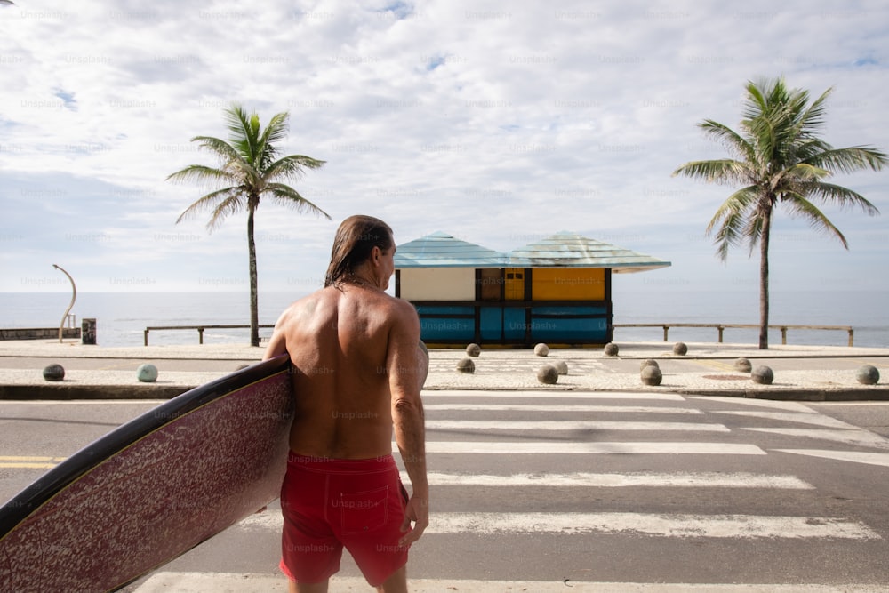 a man walking across a street holding a surfboard