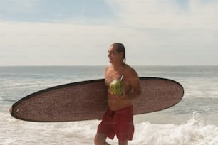 um homem segurando uma prancha de surf e uma maçã andando no oceano