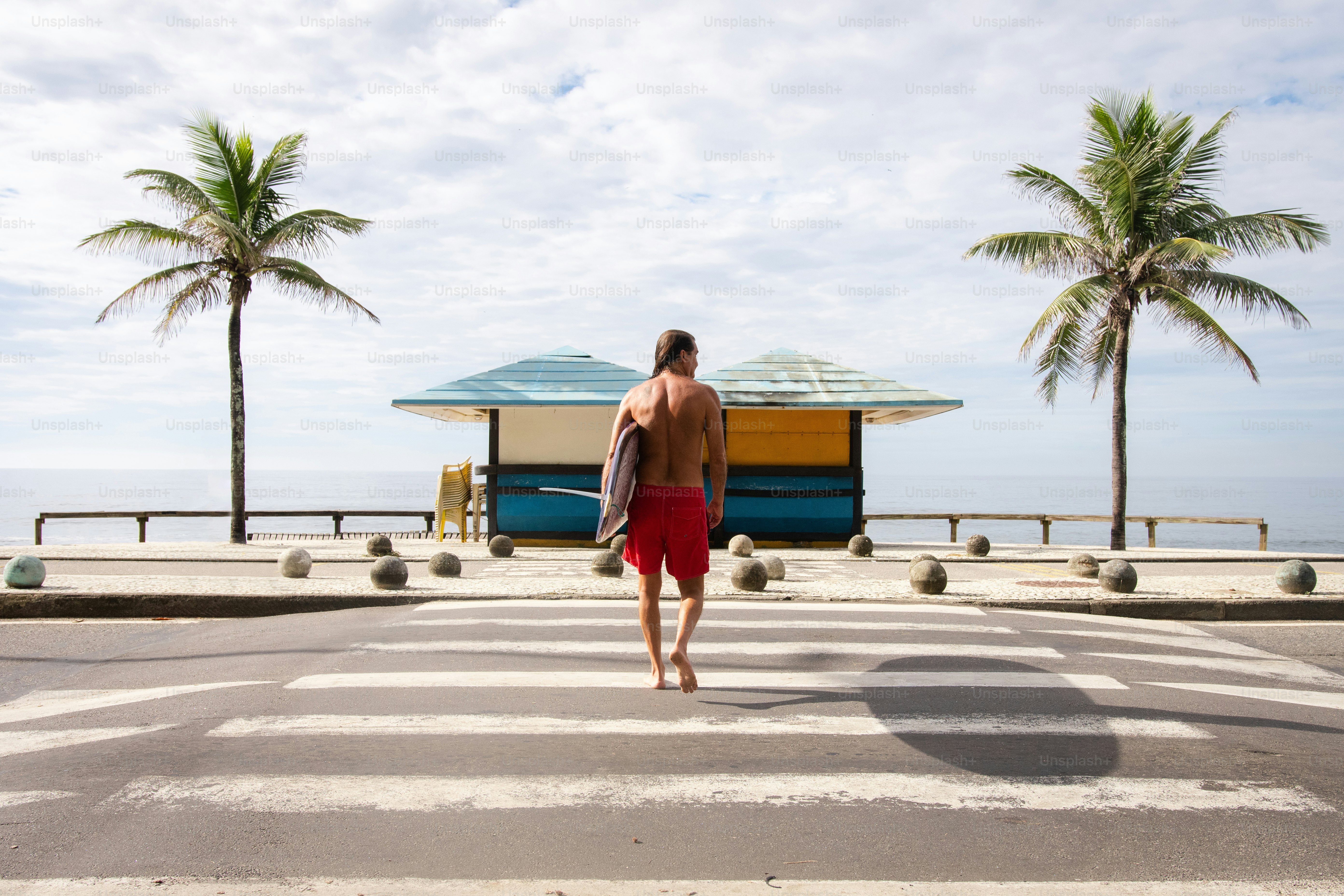 a man walking across a street holding a surfboard