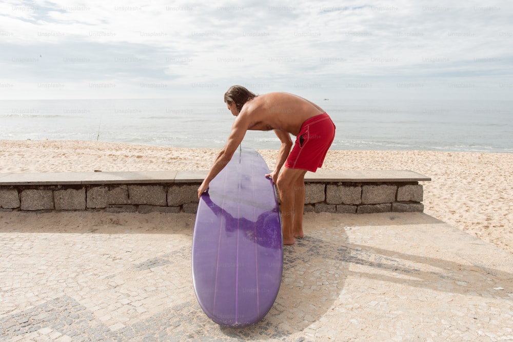 Un hombre parado junto a una tabla de surf púrpura en una playa