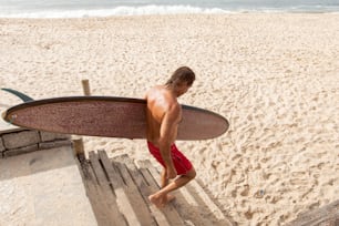 um homem sem camisa carregando uma prancha de surf em uma praia