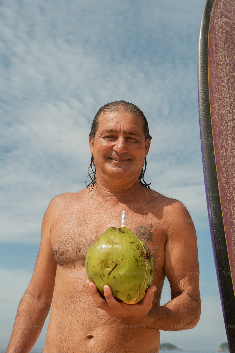 Un hombre sosteniendo un coco verde junto a una tabla de surf