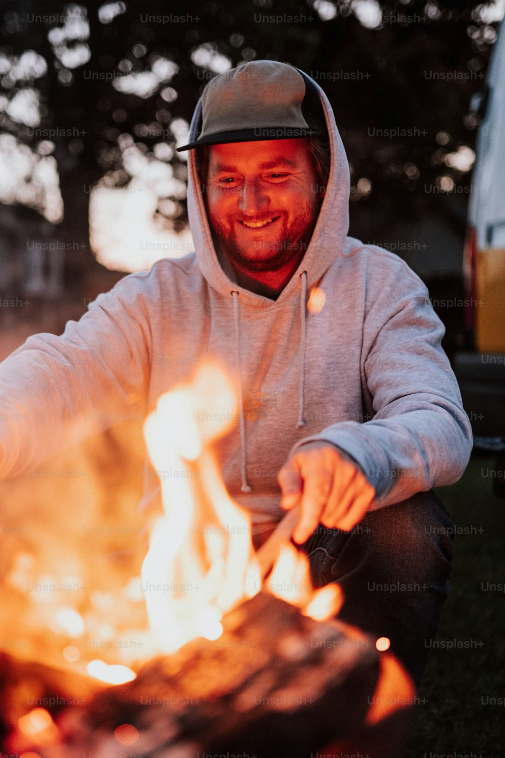 a man in a hoodie sitting in front of a fire