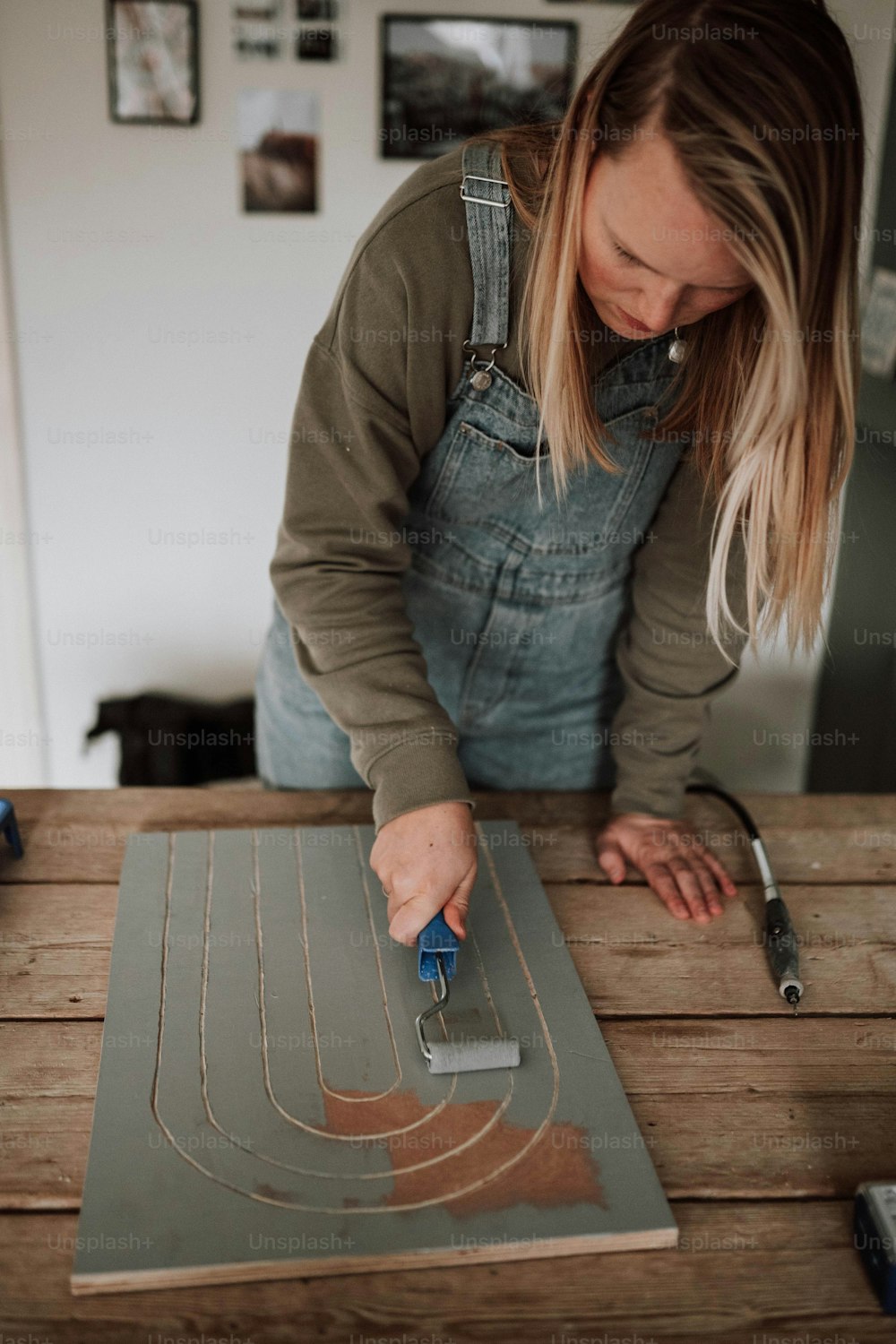 a woman in overalls painting a piece of wood