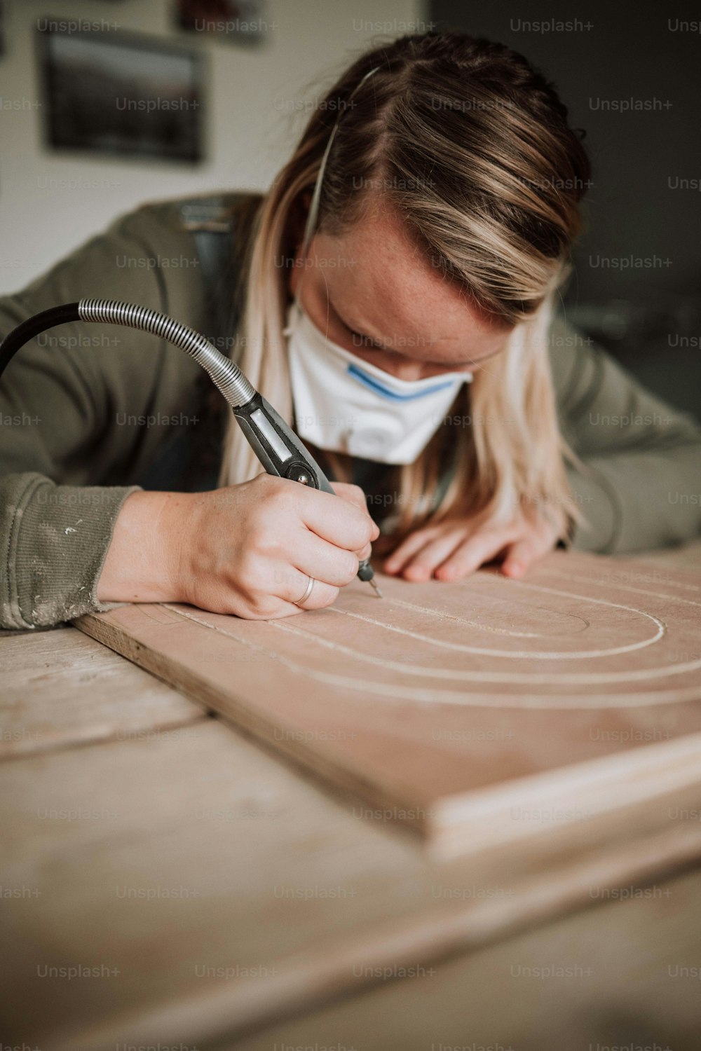 Eine Frau trägt eine Gesichtsmaske, während sie an einem Stück Holz arbeitet