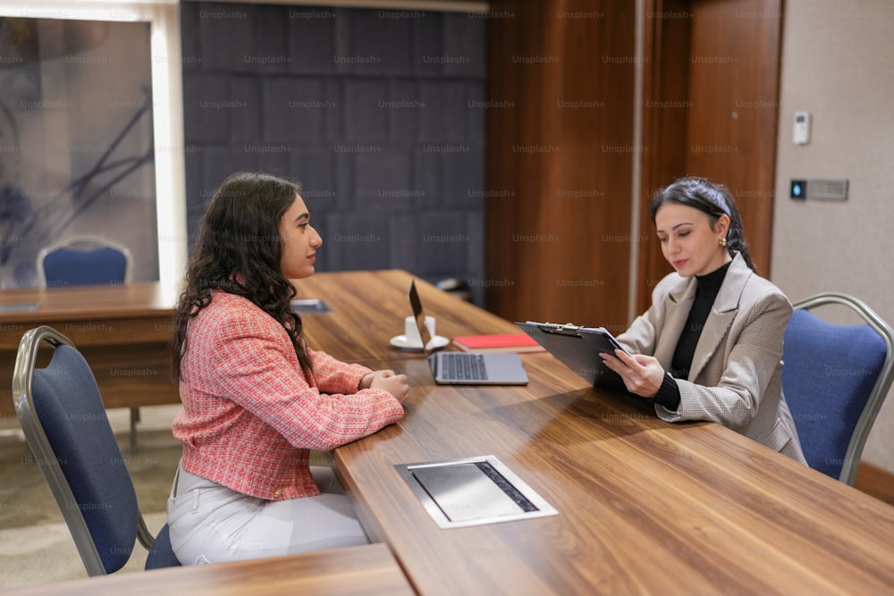 two women sitting at a table with a tablet