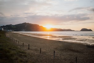 the sun is setting on the beach near the water