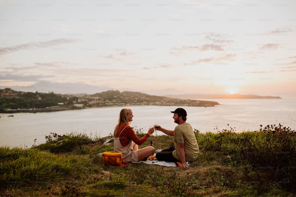 a man and a woman sitting on a hill next to a body of water