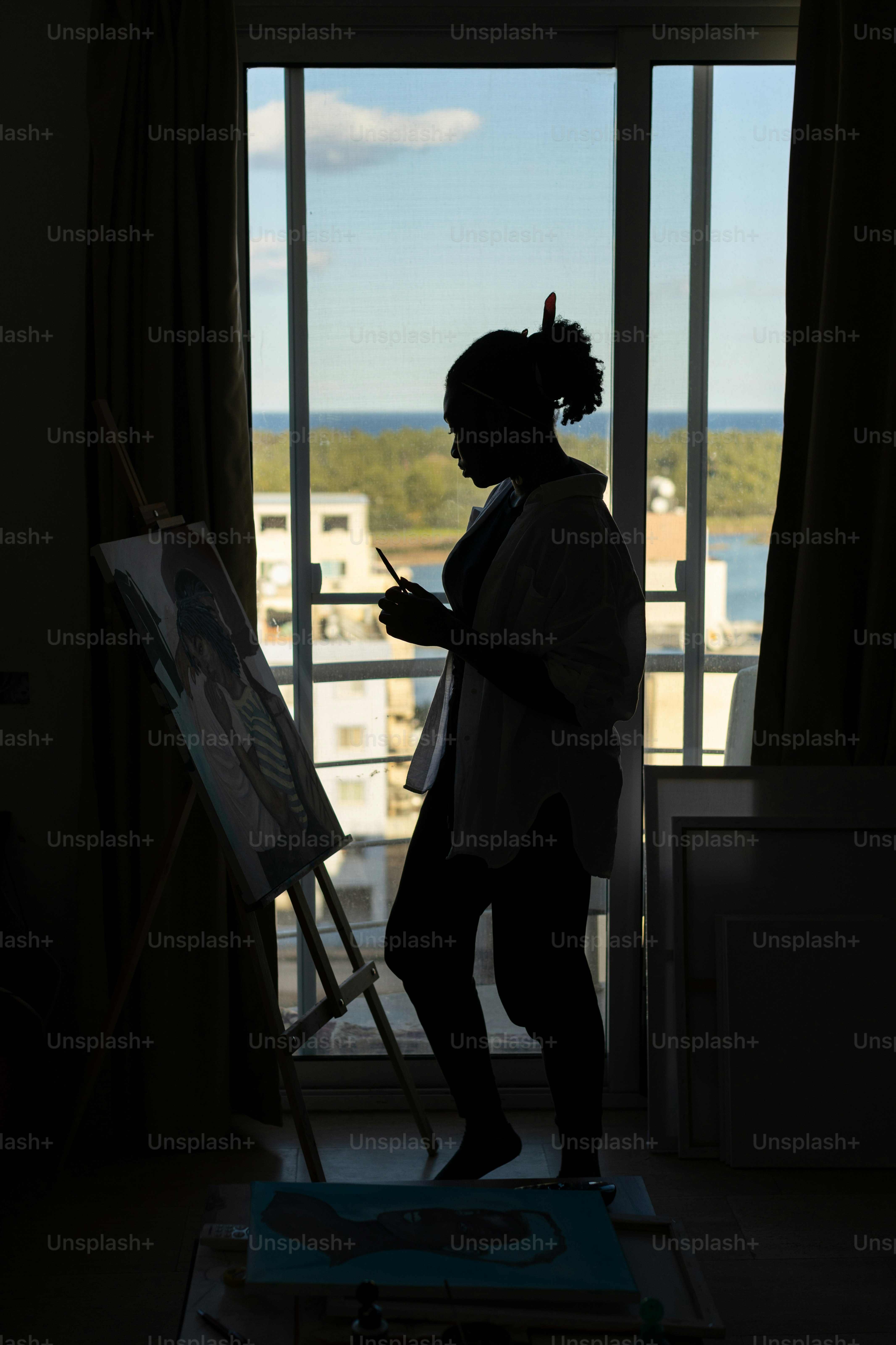 a woman standing in front of a window holding a paintbrush