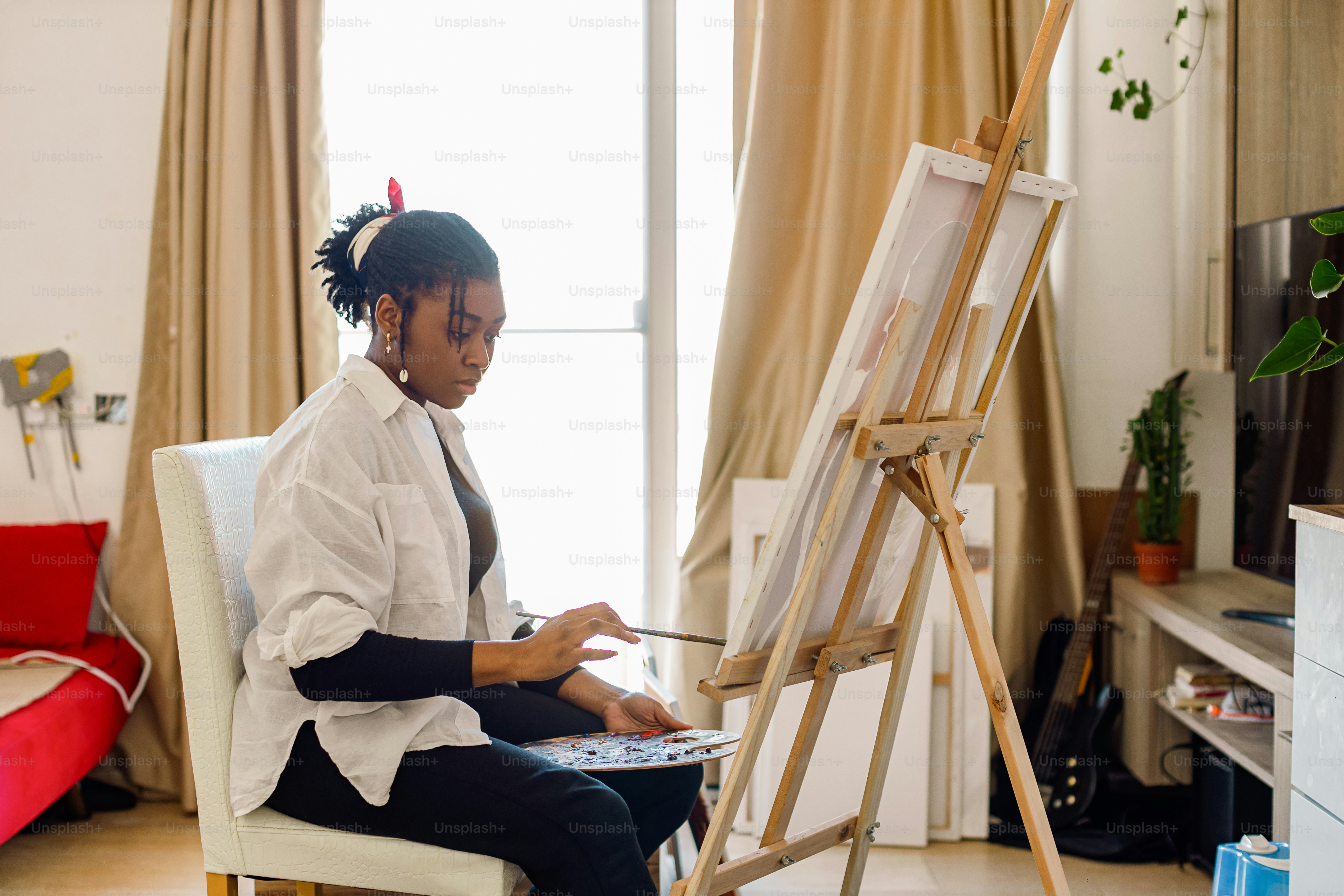 a woman sitting in a chair painting on an easel
