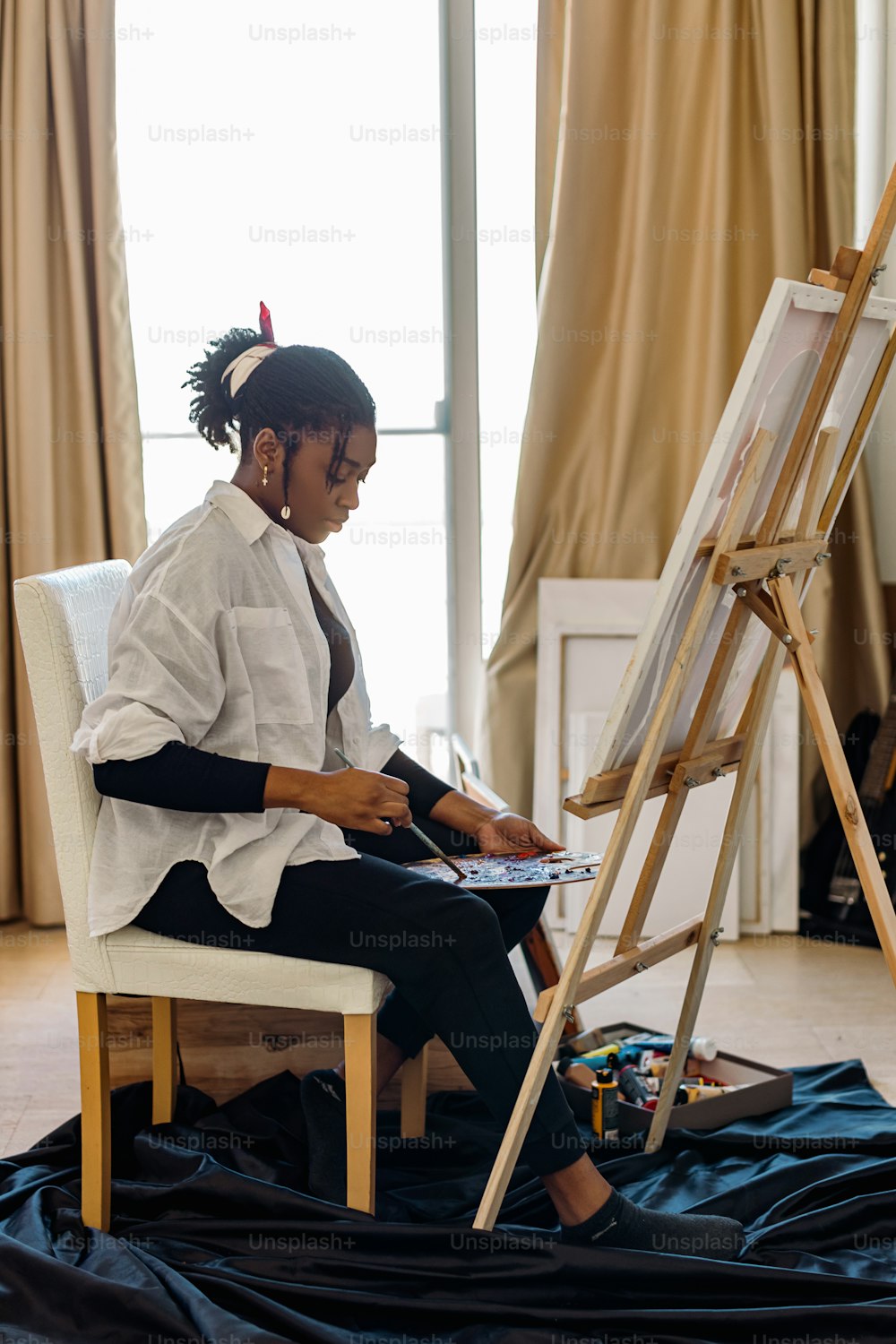 a woman sitting in a chair painting on a canvas