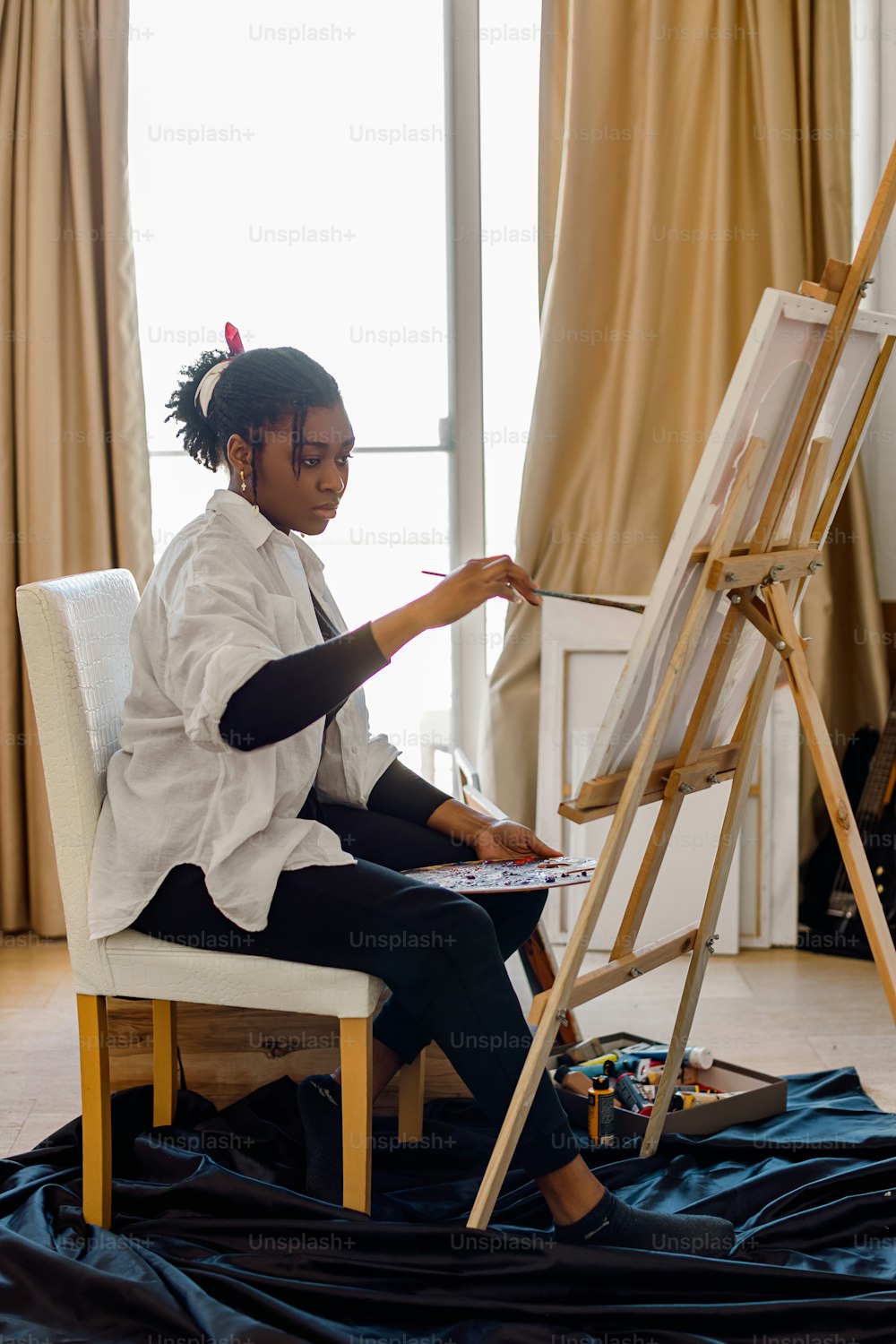 a woman sitting on a chair painting on an easel