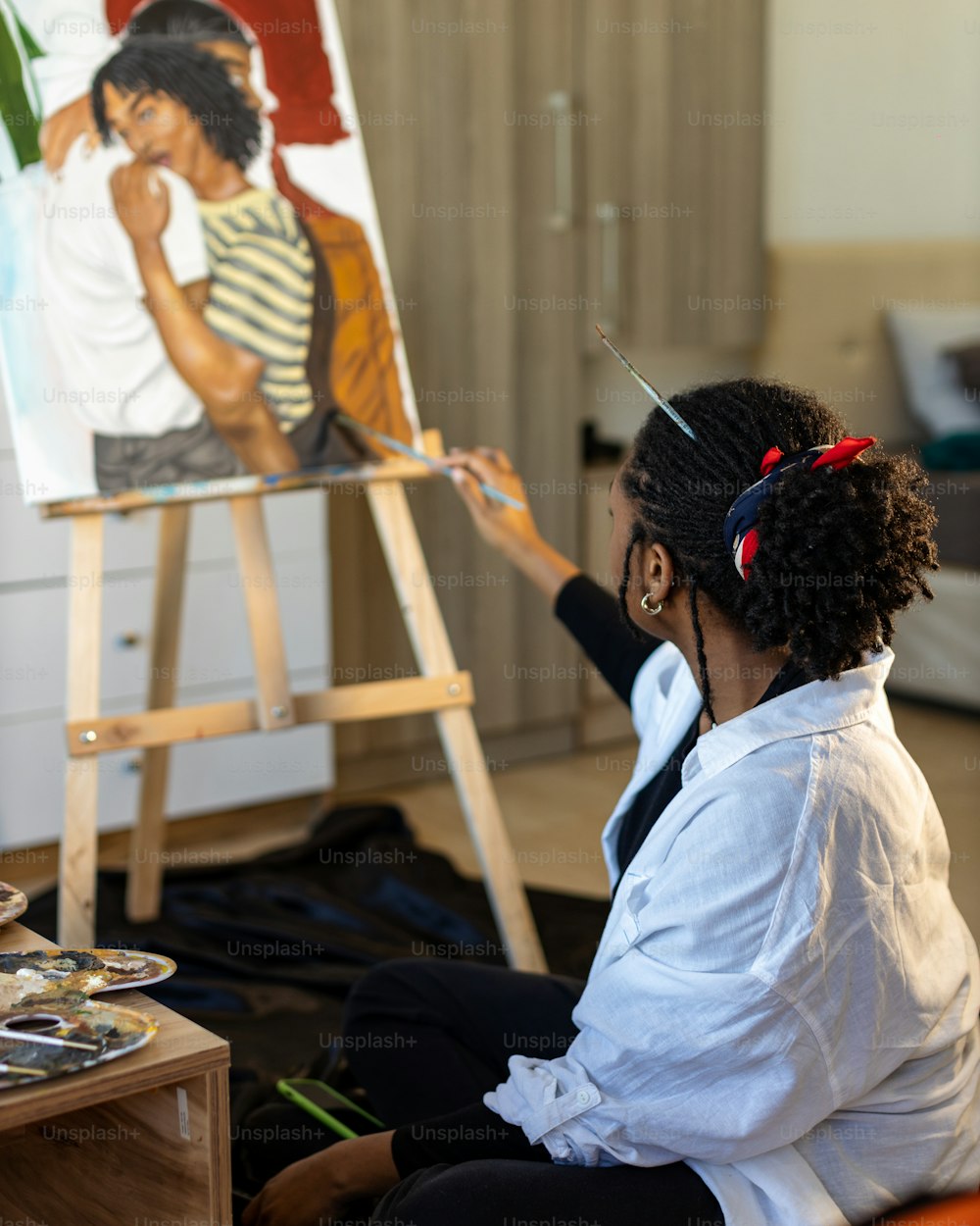 uma mulher sentada na frente de uma pintura em um cavalete