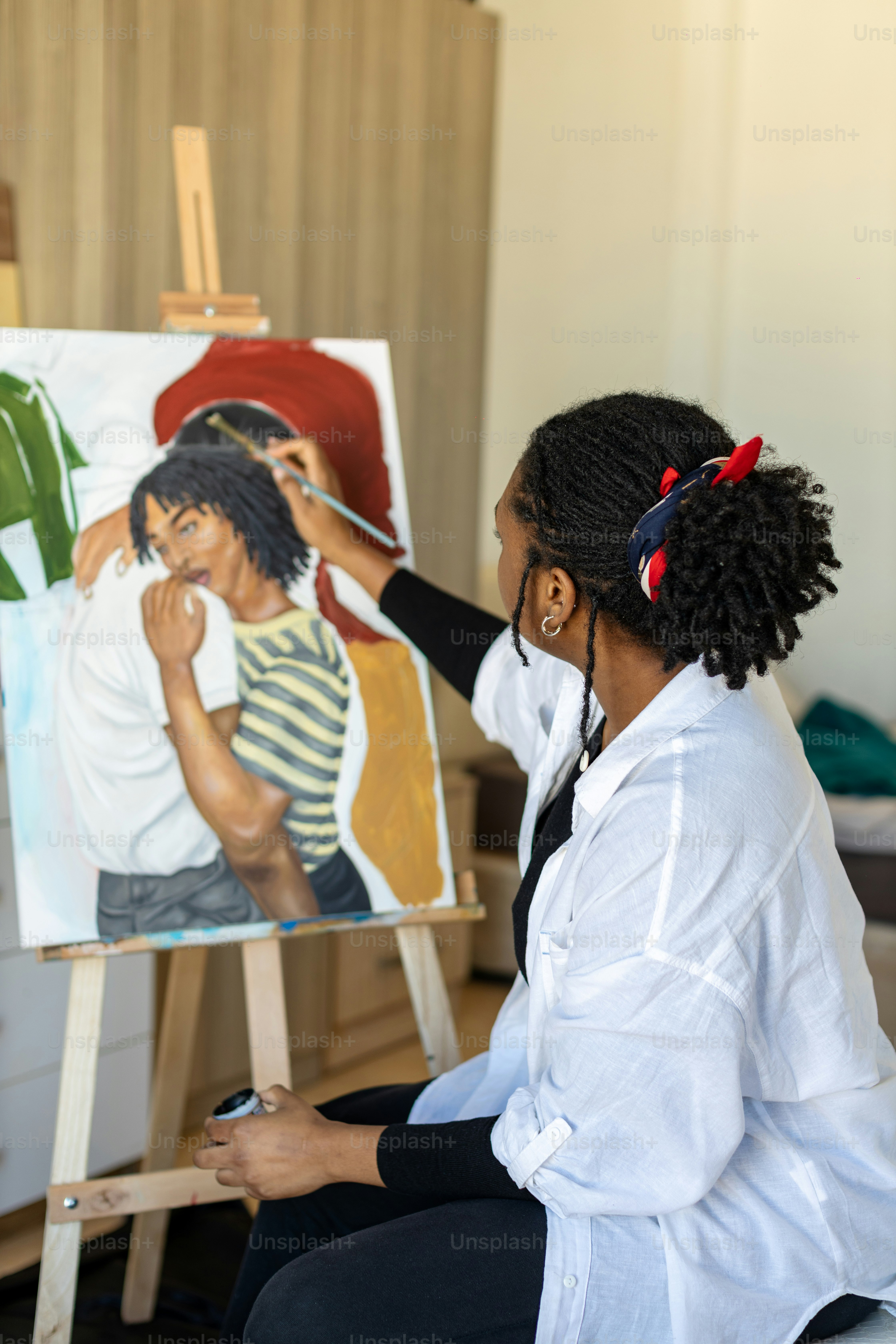 a woman sitting in front of a painting on a easel