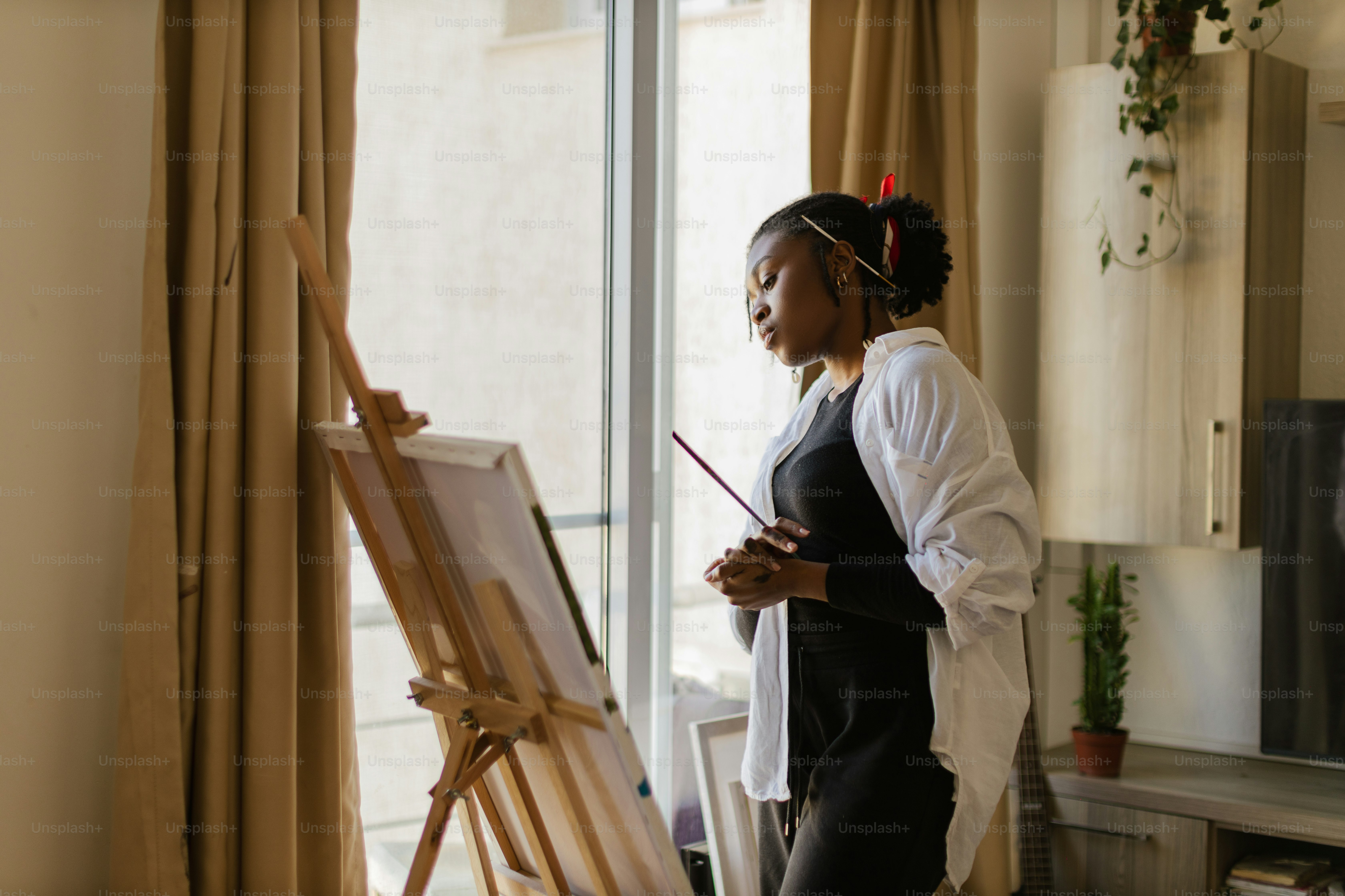 A woman standing in front of a painting easel photo – Painting Image on ...