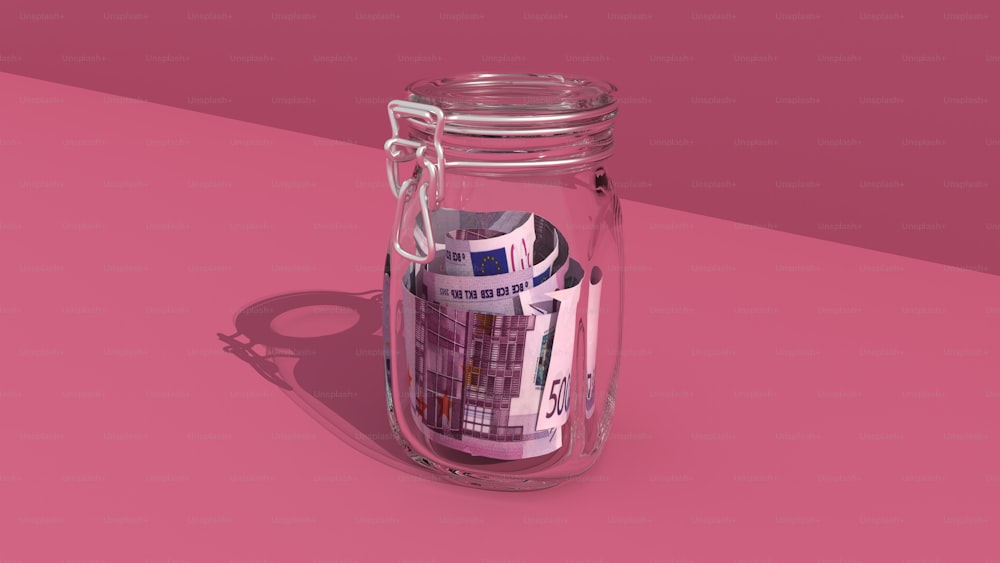 ピンクの表面の上に座っているお金で満たされた瓶