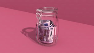 a jar filled with money sitting on top of a pink surface