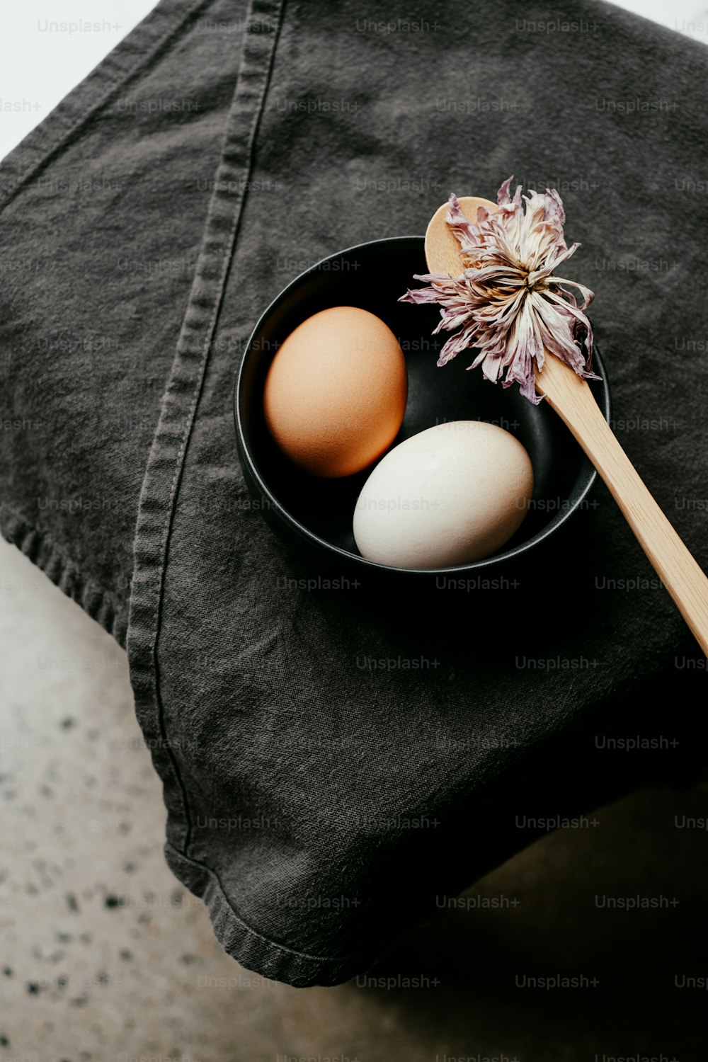 two eggs in a black bowl with a wooden spoon
