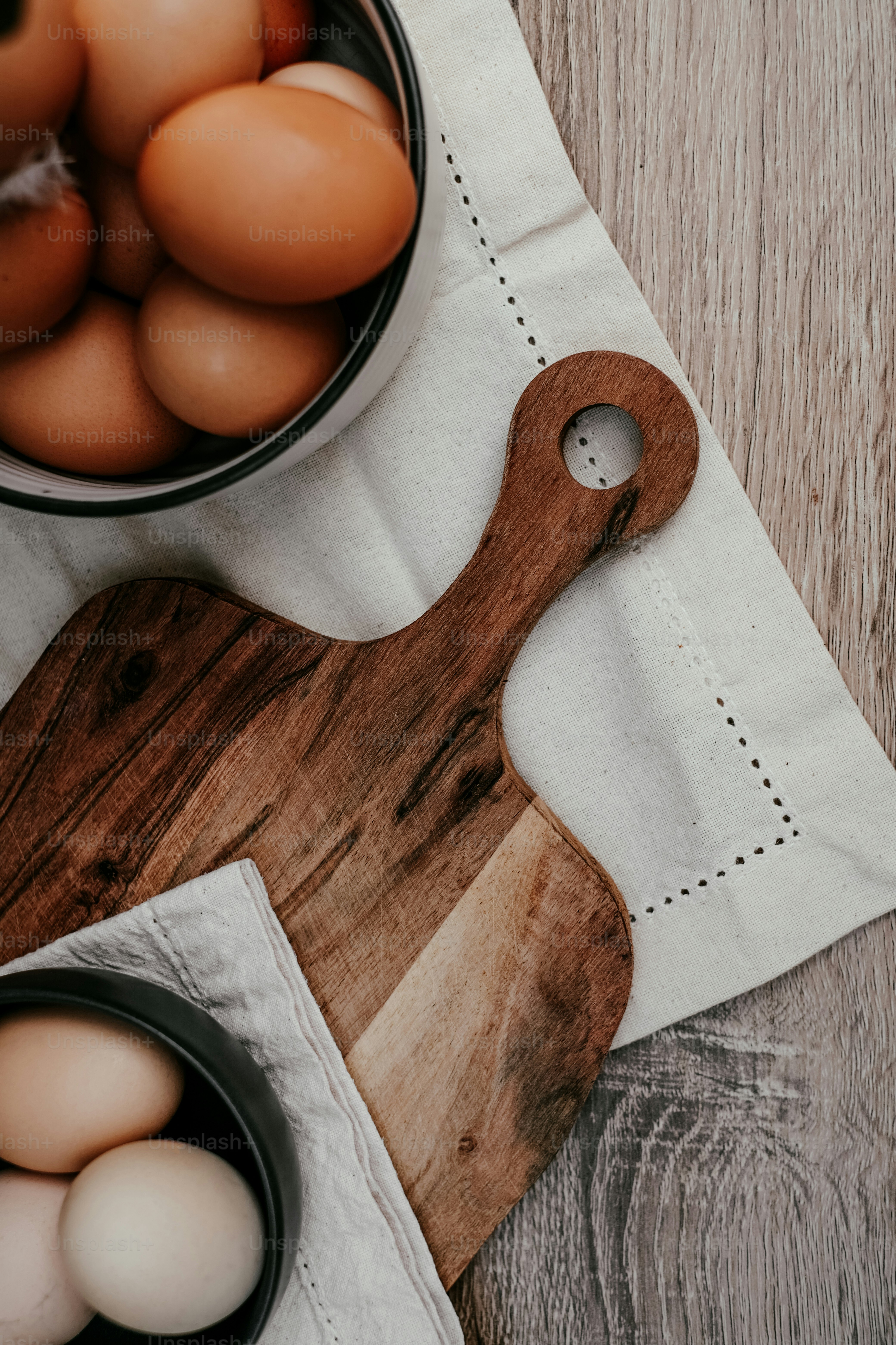 a wooden cutting board topped with eggs next to a bowl of eggs