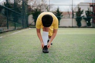 a man in a yellow shirt tying his shoes on a tennis court