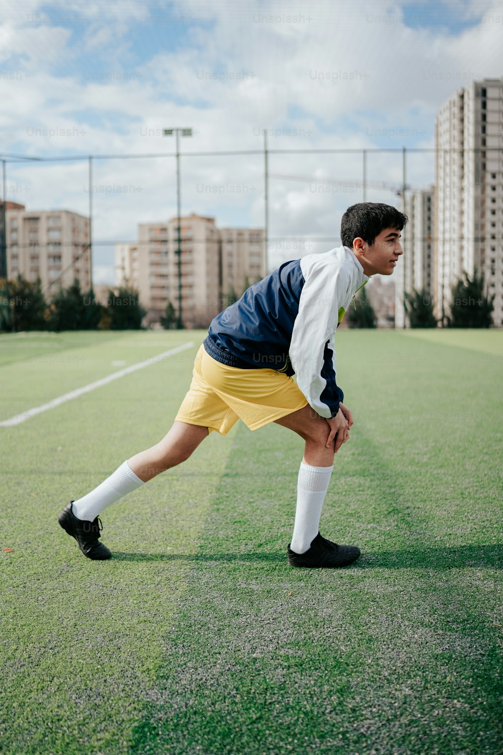 a young man in yellow shorts and a blue jacket on a soccer field