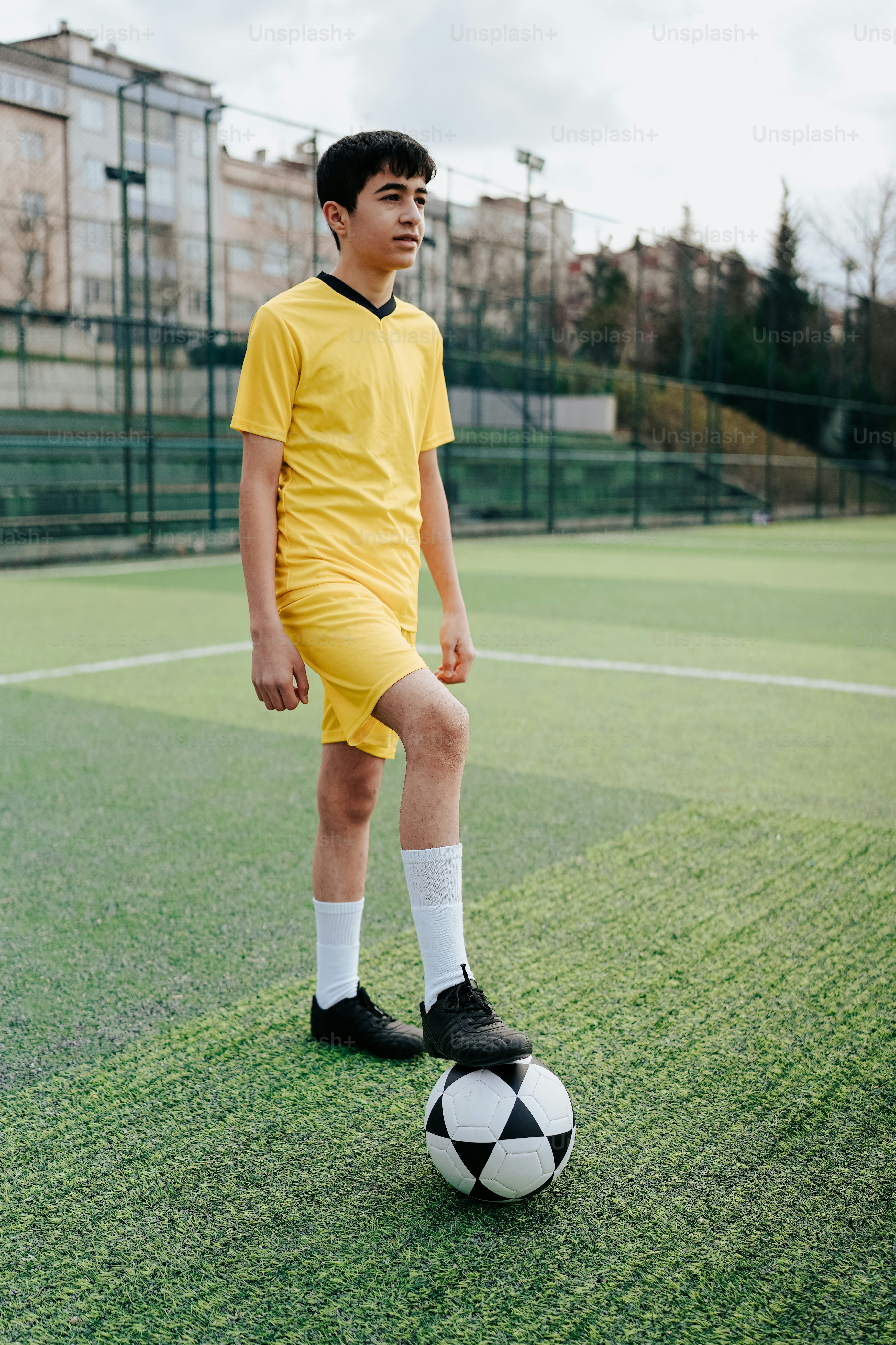 a young boy in a yellow uniform standing on a soccer ball