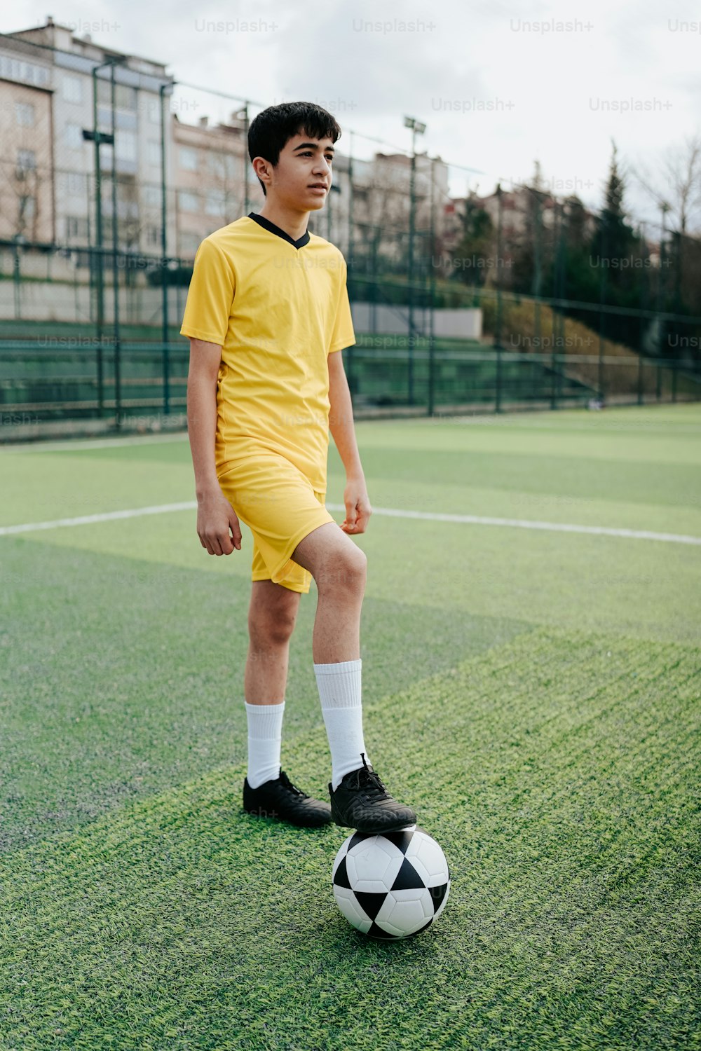 a young boy in a yellow uniform standing on a soccer ball