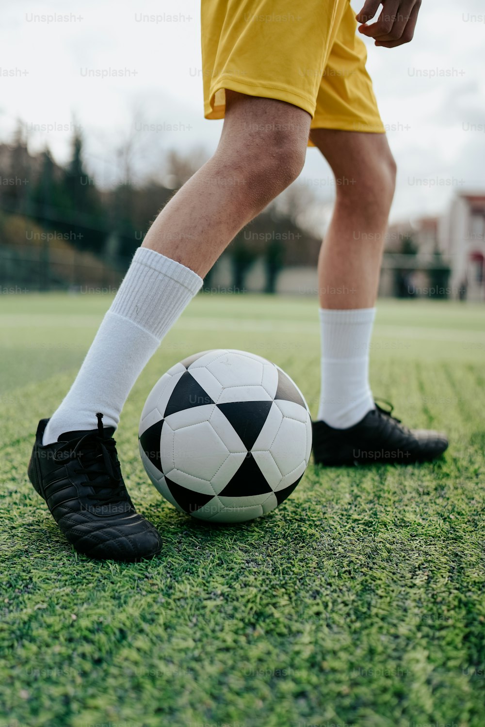 Una persona con pantalones cortos amarillos y zapatos negros pateando una pelota de fútbol