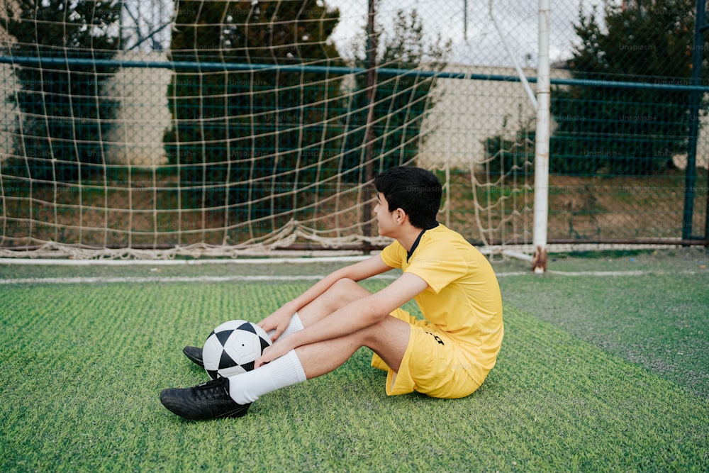 a boy sitting on the ground with a soccer ball