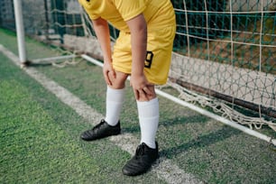 サッカーのユニフォームを着た少年がサッカーゴールの前にひざまずく