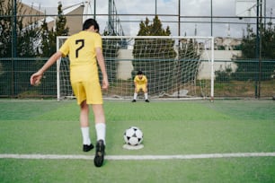 um menino jovem chutando uma bola de futebol em um campo de futebol