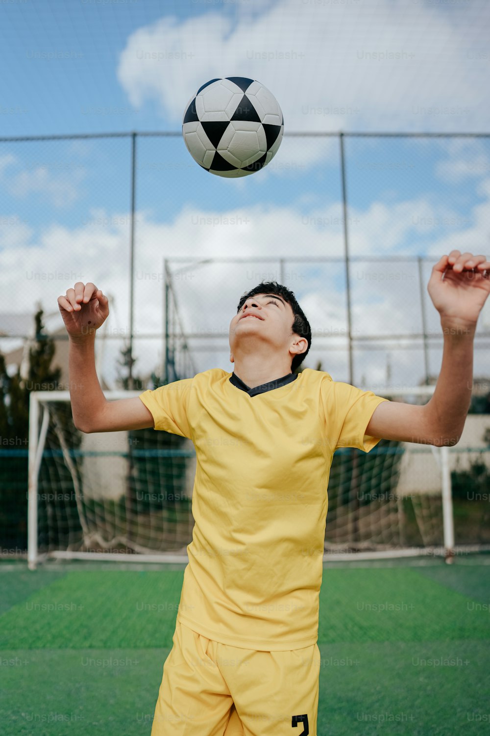a young man in a yellow uniform reaching up to catch a soccer ball