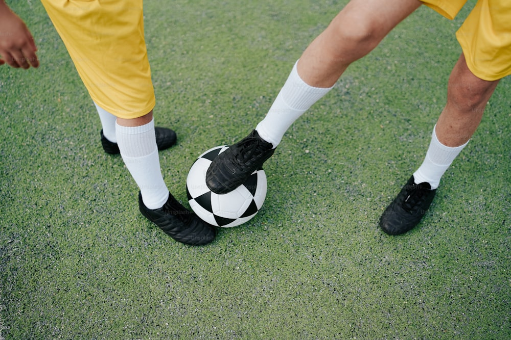 a close up of two soccer players with their feet on a soccer ball