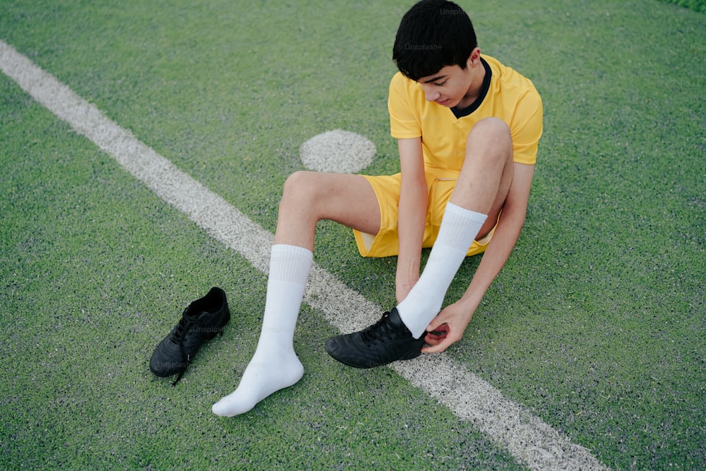a young man sitting on a soccer field with his foot on the ground