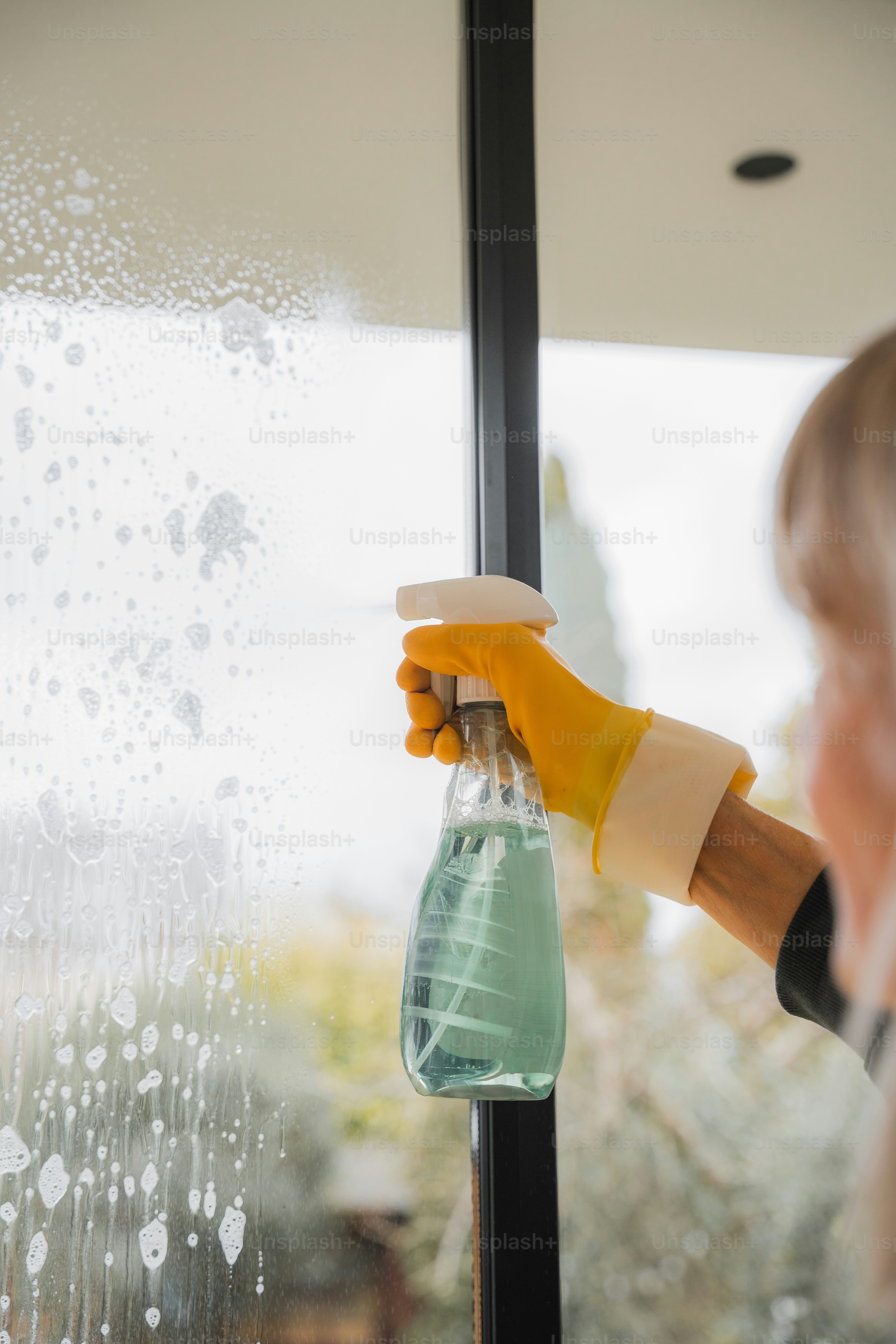 A person in yellow gloves and rubber gloves holding a bottle of water ...