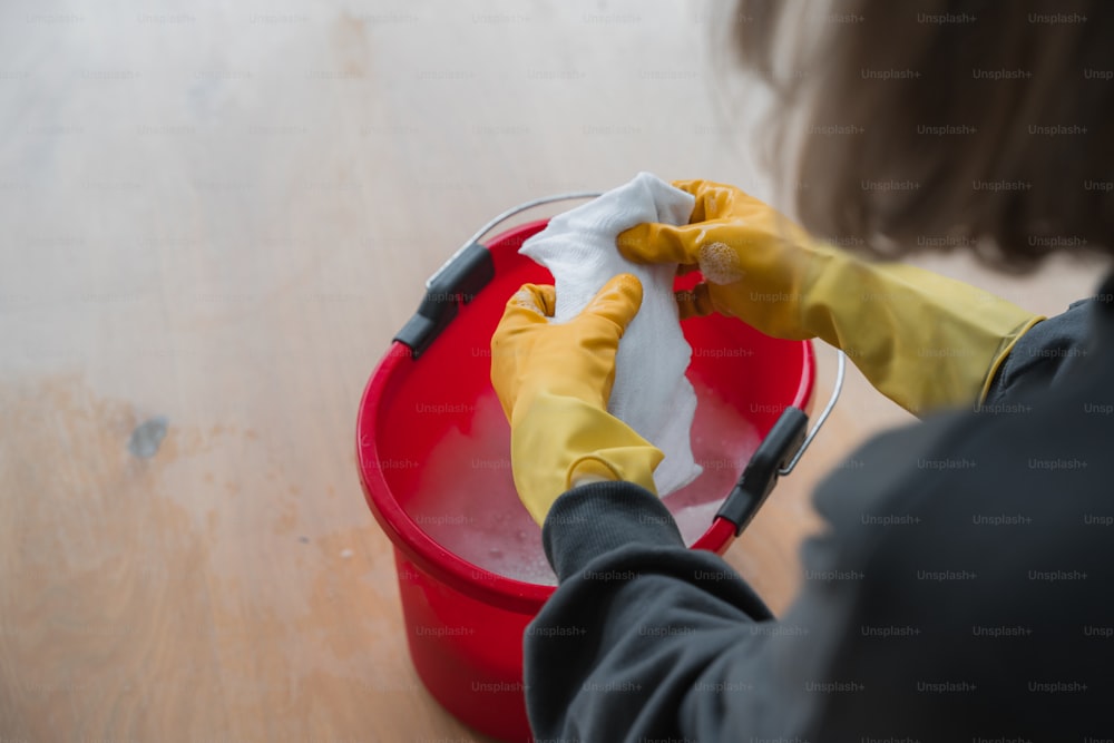 uma mulher que limpa um balde vermelho com luvas amarelas