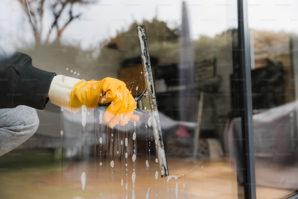 a person wearing yellow gloves is washing a window