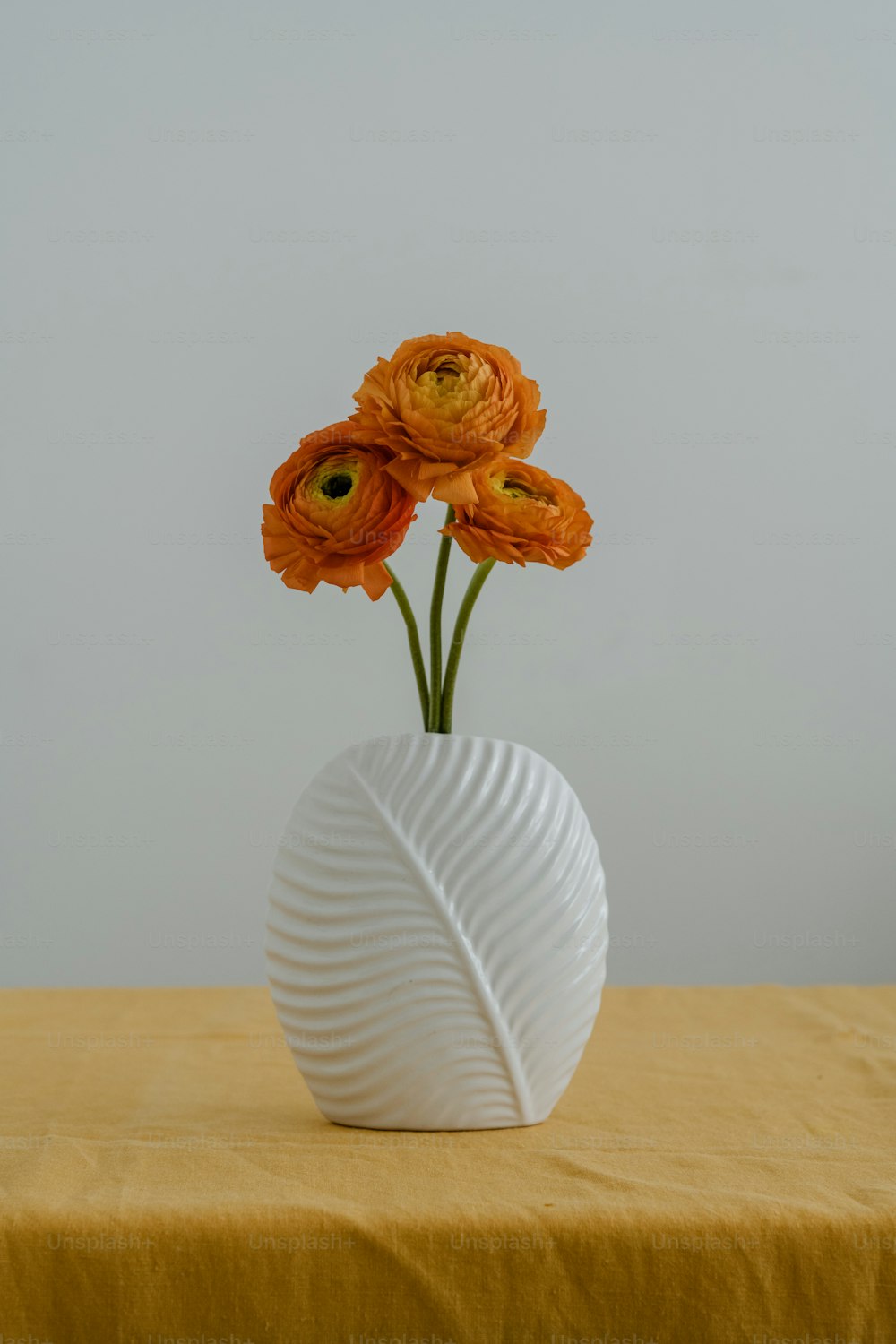 Un jarrón blanco con tres flores naranjas