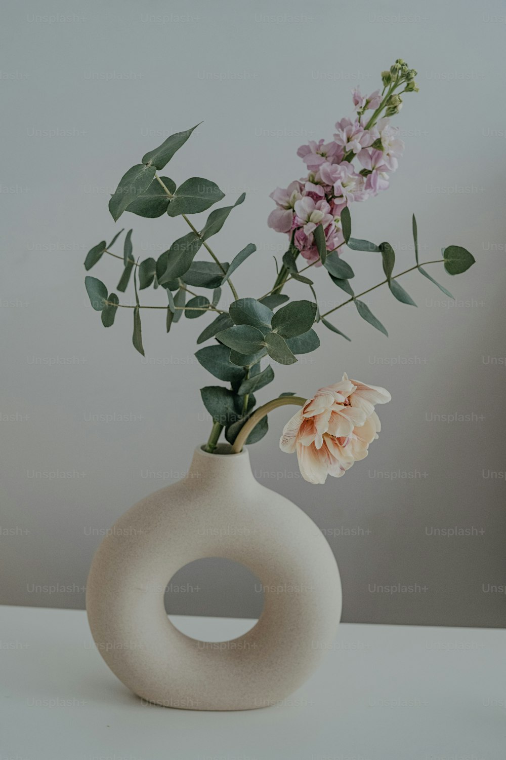 eine weiße Vase mit Blumen darauf auf einem Tisch