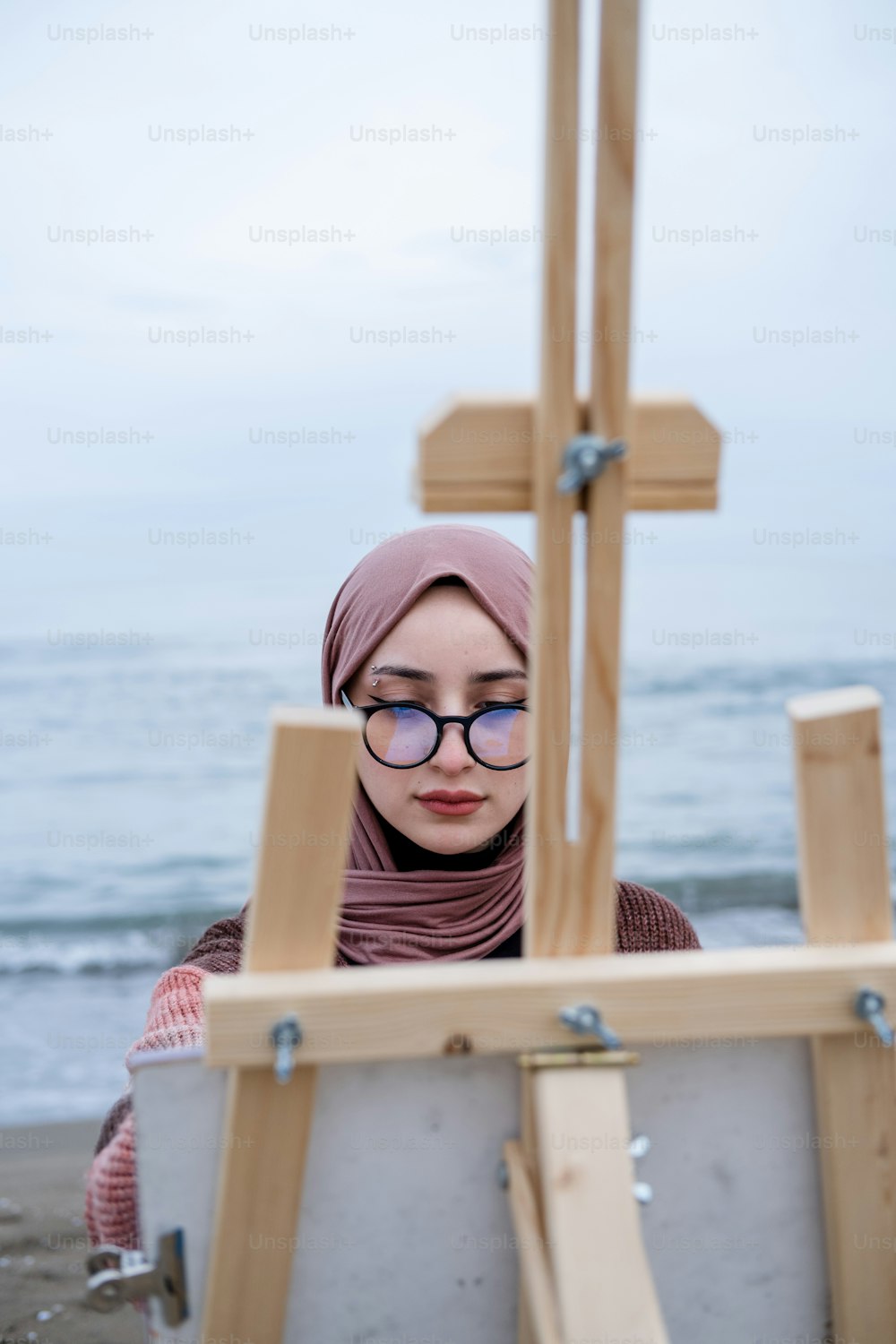 a woman wearing glasses and a hijab is looking at a painting easel