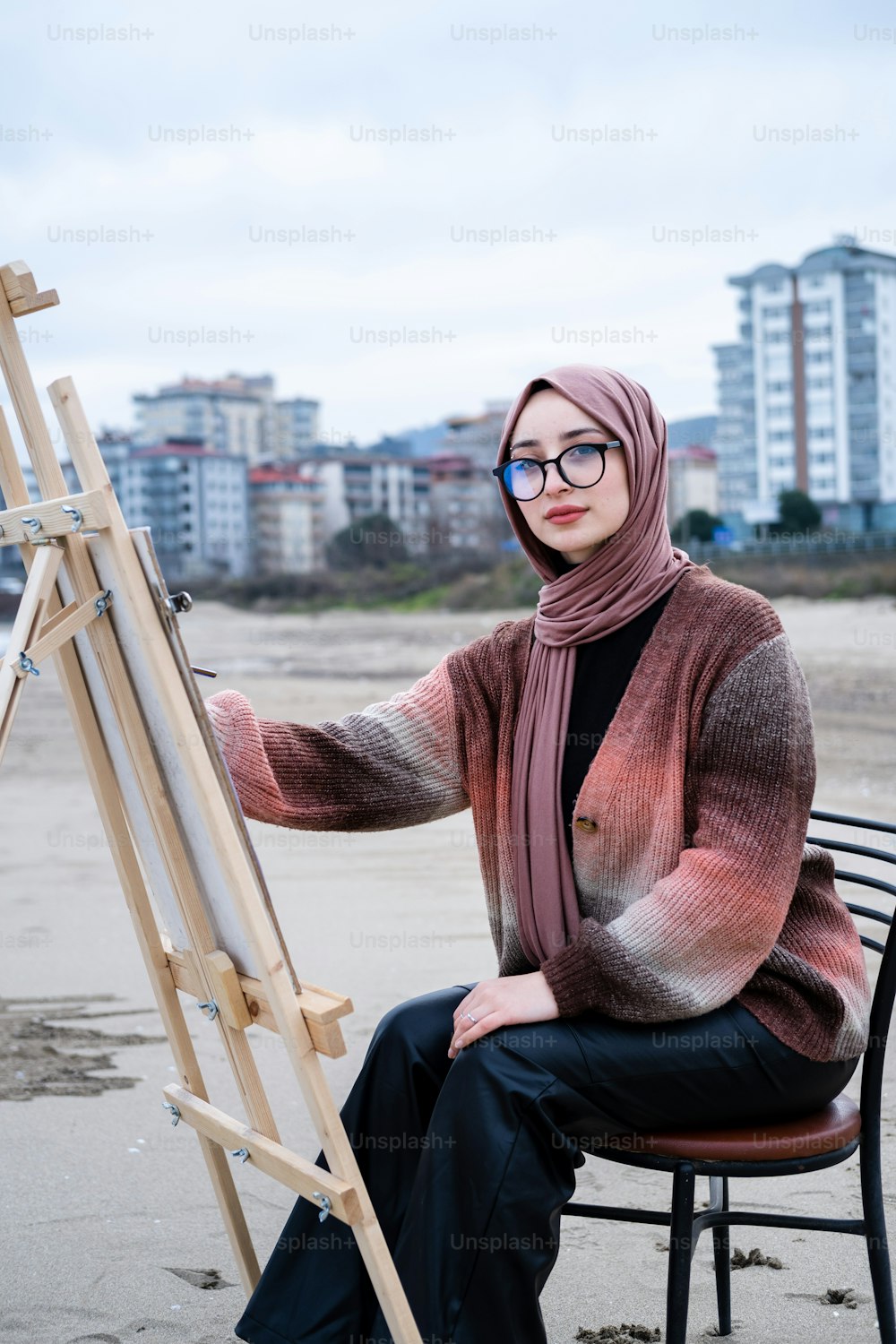 Eine Frau im Hijab sitzt auf einem Stuhl mit einer Staffelei