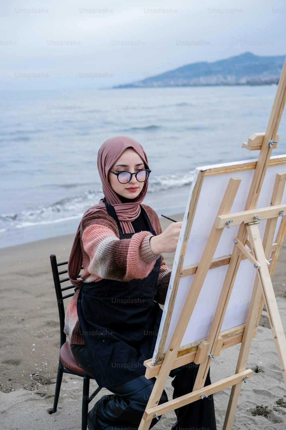 히잡을 쓴 여자가 해변에서 그림을 그리고 있다