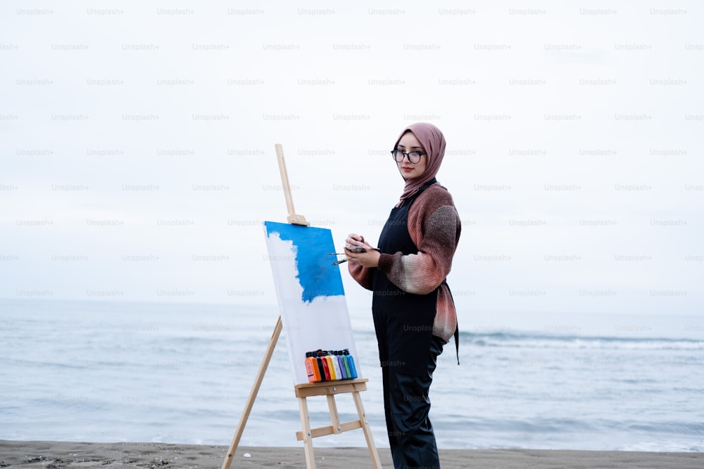 a woman standing on a beach next to an easel