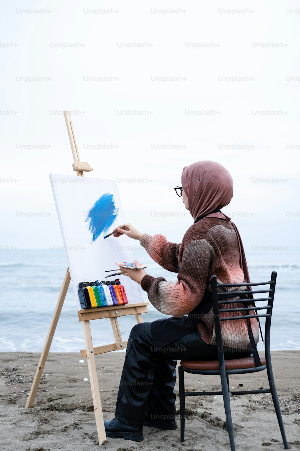 a man sitting in a chair painting on a canvas