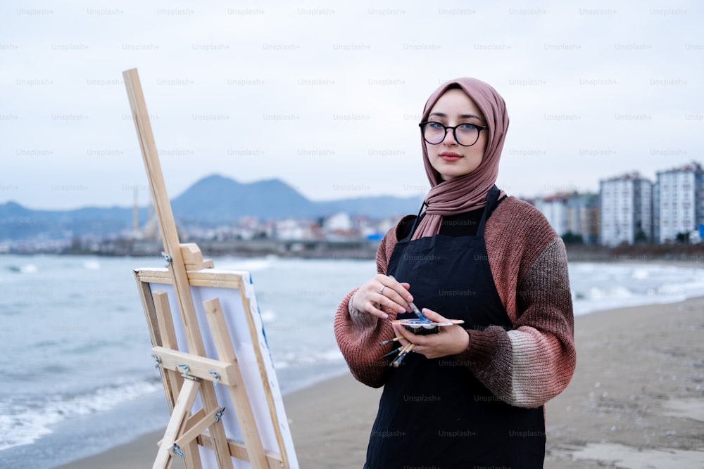 a woman standing next to a easel on a beach
