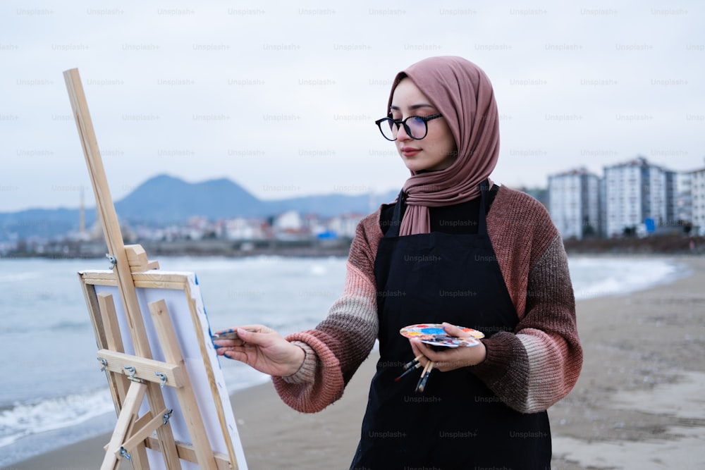 a woman in a hijab is painting on the beach