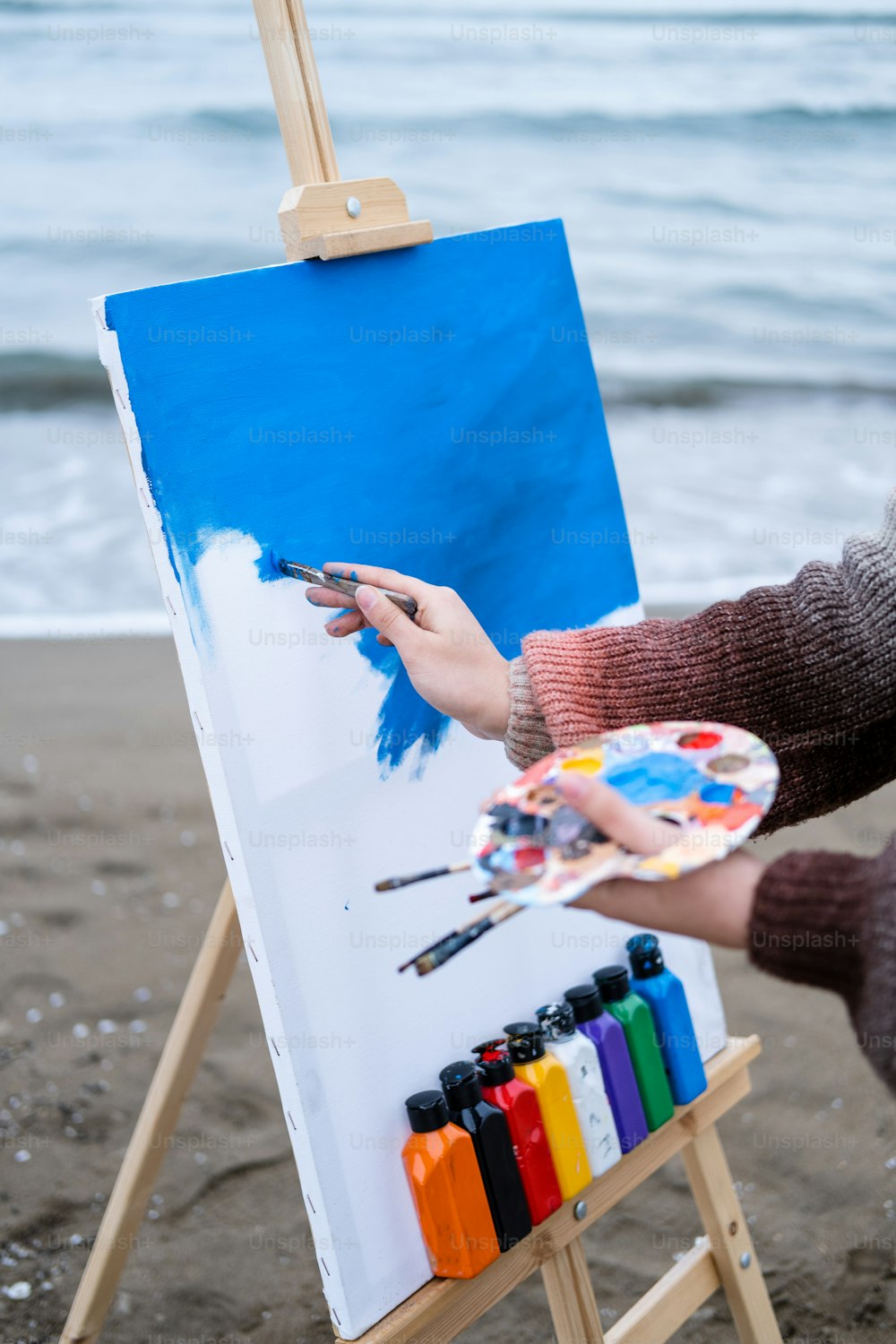 a person holding a paintbrush and painting a picture on a easel