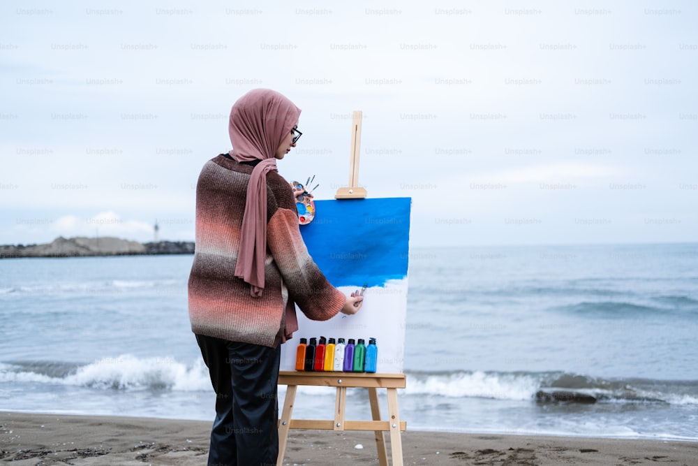 a woman in a hijab painting on a beach